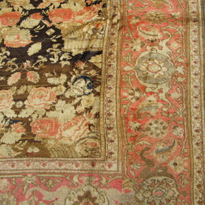 Detailed view of a heavily worn rug showing brown, gold, and pink floral patterns in the field and border.