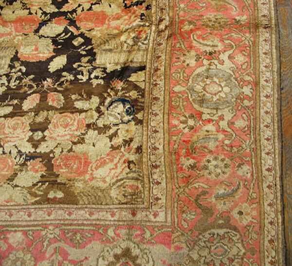 Detailed view of a heavily worn rug showing brown, gold, and pink floral patterns in the field and border.