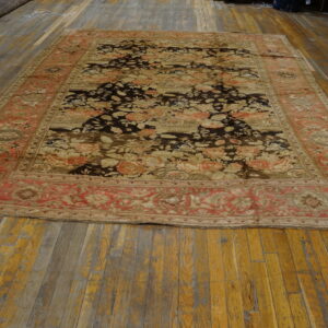 Floral area rug with a dark field and faded red border, lying flat on distressed wood floors.