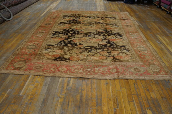 Floral area rug with a dark field and faded red border, lying flat on distressed wood floors.