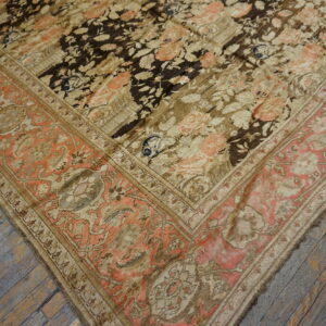 Close-up of a dark floral rug with coral border details resting on rustic gray wooden planks.