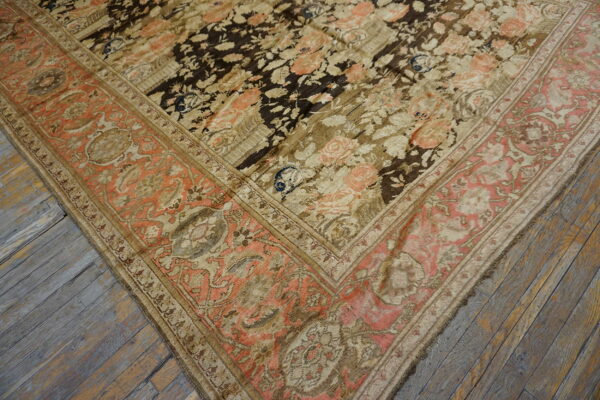 Close-up of a dark floral rug with coral border details resting on rustic gray wooden planks.