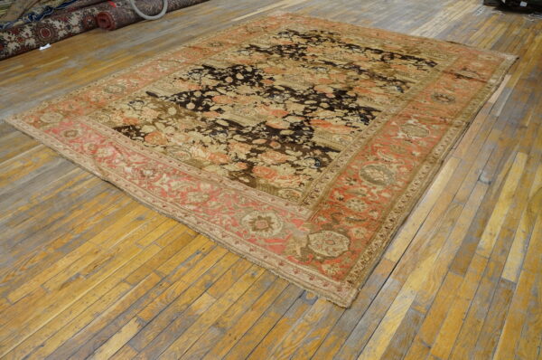 Ornate low-pile rug in dark brown, tan, and coral sits on a weathered plank wood floor.