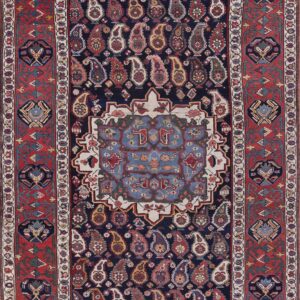 Traditional rug featuring a navy field of multicolored paisley motifs framed by a wide red geometric border.