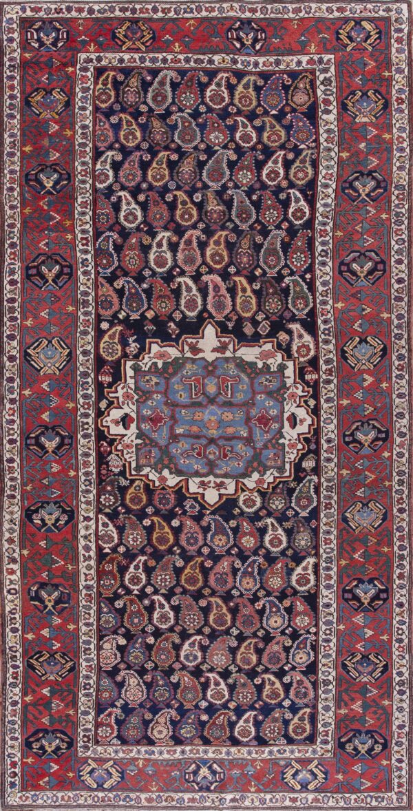 Traditional rug featuring a navy field of multicolored paisley motifs framed by a wide red geometric border.