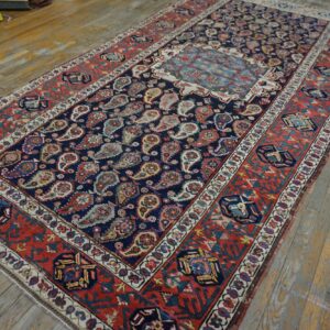 Navy and red rug featuring dense paisley patterns and a light blue medallion on worn wood floors.