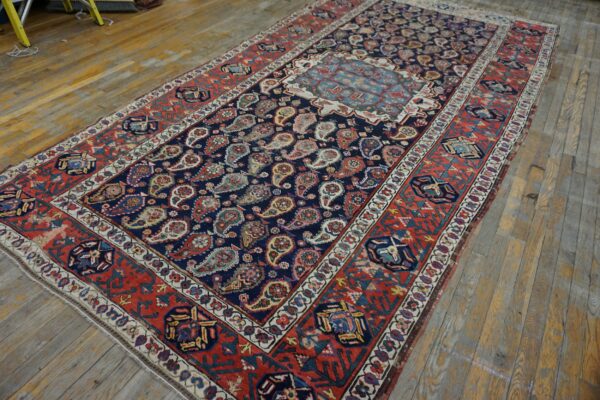 Navy and red rug featuring dense paisley patterns and a light blue medallion on worn wood floors.