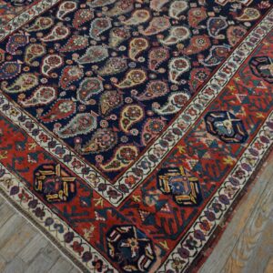 Navy and red rug featuring detailed paisley motifs and geometric borders on worn wooden floors.