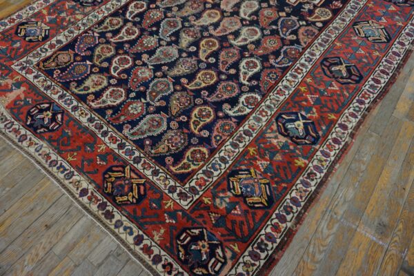 Navy and red rug featuring detailed paisley motifs and geometric borders on worn wooden floors.