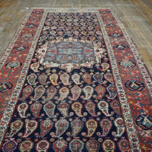 Low-pile runner rug with a navy paisley field, light blue medallion, and rust geometric borders on wood flooring.
