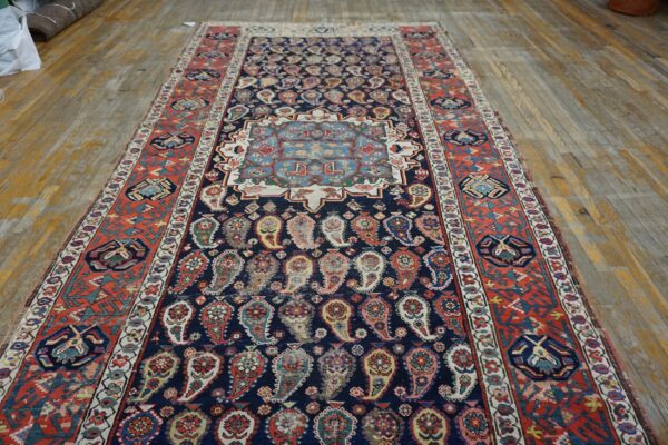 Low-pile runner rug with a navy paisley field, light blue medallion, and rust geometric borders on wood flooring.