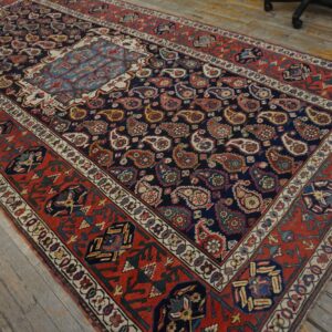 Navy rug with allover paisley design and a wide red tribal border on weathered plank flooring.