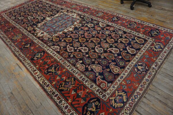 Navy rug with allover paisley design and a wide red tribal border on weathered plank flooring.