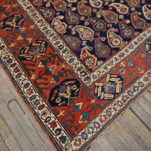 Navy and red patterned rug featuring paisley motifs and geometric borders on weathered gray hardwood flooring.