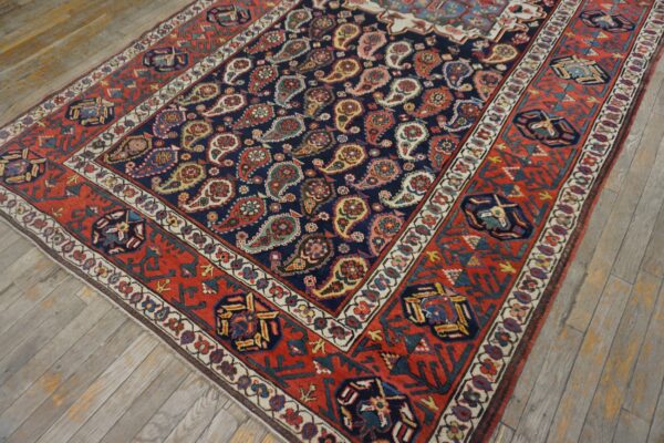 Navy and red patterned rug with a detailed paisley design lies on distressed light wood plank floors.