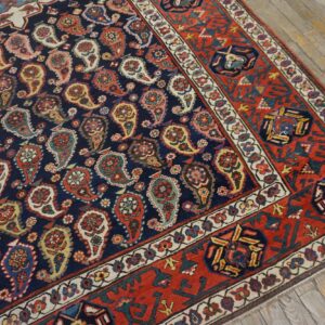 Navy rug with colorful paisley motifs and a red geometric border on distressed wood flooring.