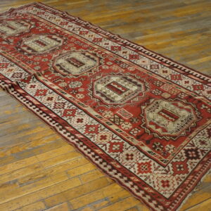 Red and cream geometric runner rug with three medallions on worn wood plank flooring.