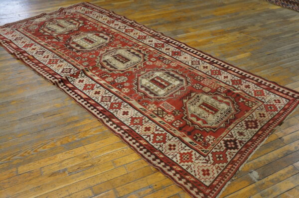 Red and cream geometric runner rug with three medallions on worn wood plank flooring.
