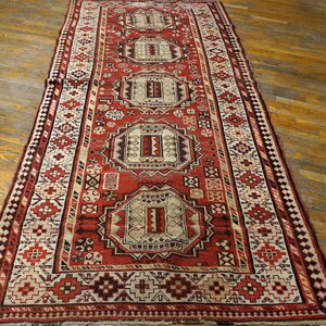 Geometric runner rug in red, cream, and dark brown features central medallions on wooden flooring.