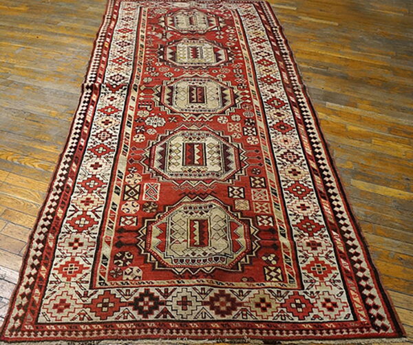 Geometric runner rug in red, cream, and dark brown features central medallions on wooden flooring.