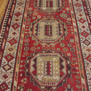Red and cream runner with geometric medallions and intricate borders on light brown hardwood floors.