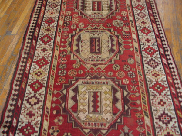 Red and cream runner with geometric medallions and intricate borders on light brown hardwood floors.
