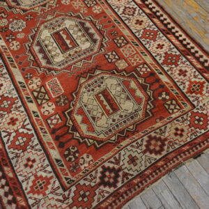 A red, tan, and brown geometric tribal rug with central medallions rests on weathered gray wooden plank flooring.