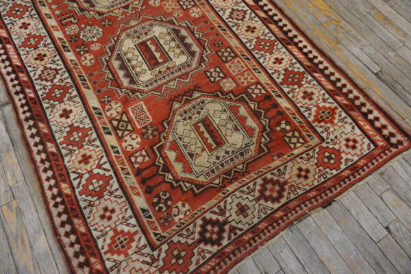A red, tan, and brown geometric tribal rug with central medallions rests on weathered gray wooden plank flooring.