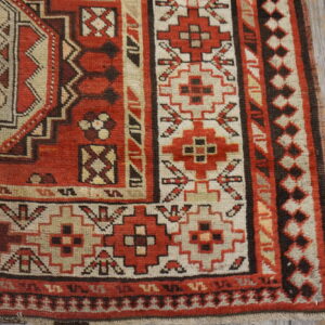 Red, cream, and brown geometric patterned rug corner detail rests on weathered gray wood planks.