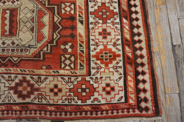 Red, cream, and brown geometric patterned rug corner detail rests on weathered gray wood planks.