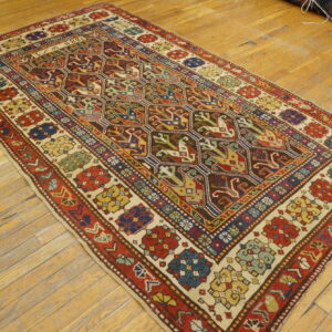 Multi-colored low-pile rug with geometric patterns and red borders displayed on light brown wood flooring.