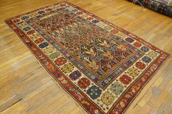 Multi-colored low-pile rug with geometric patterns and red borders displayed on light brown wood flooring.