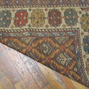 The border of a tightly woven geometric rug in red, blue, and yellow rests on distressed wood planks.