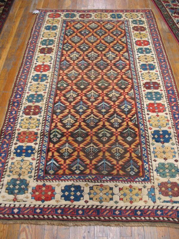 Geometric rug featuring a dark patterned field and a light border with colorful medallions rests on natural wood flooring.