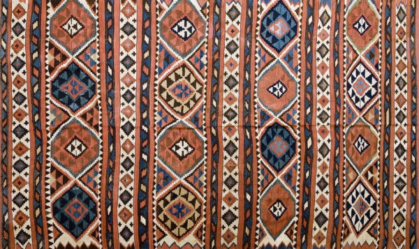 Rust and navy flatwoven rug displaying vertical columns of complex geometric diamond patterns.