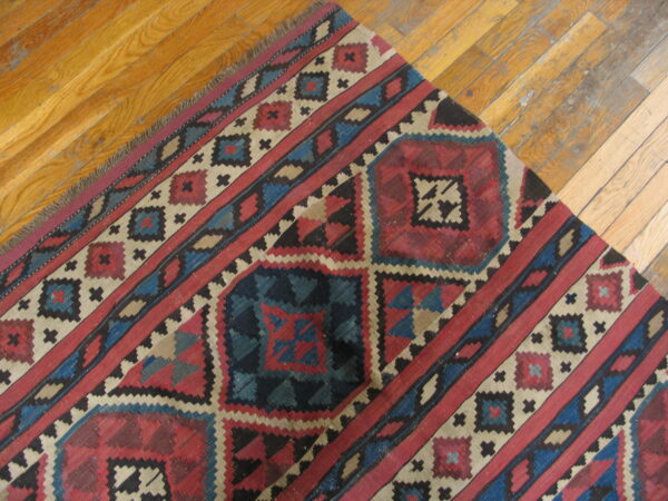Red, navy, and cream geometric rug with fringe lies diagonally across glossy wood planks.