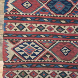 Flat-woven geometric rug in deep red, navy, and cream diamonds lying on distressed wood planks.