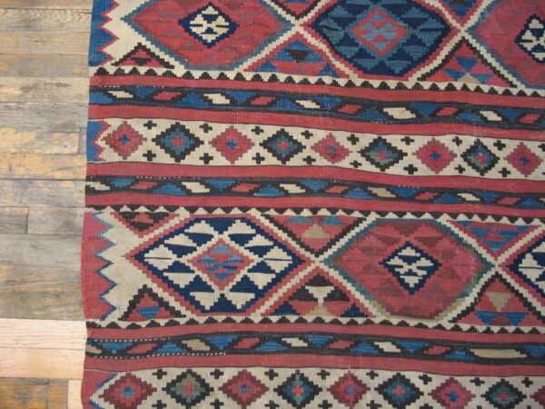 Flat-woven geometric rug in deep red, navy, and cream diamonds lying on distressed wood planks.