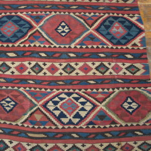 Flatweave rug with bold horizontal bands of red and blue geometric designs on light wood planks.