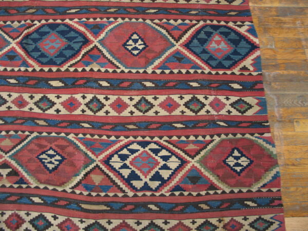 Flatweave rug with bold horizontal bands of red and blue geometric designs on light wood planks.