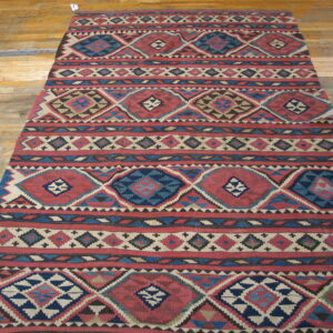 Red and indigo flatweave rug with repeating diamond patterns on distressed wood plank flooring.