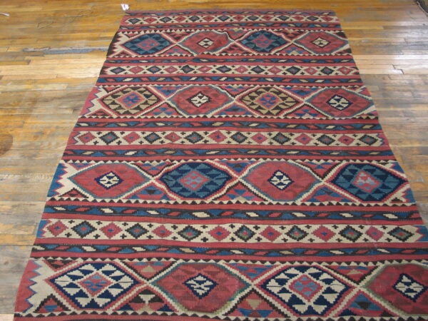 Red and indigo flatweave rug with repeating diamond patterns on distressed wood plank flooring.