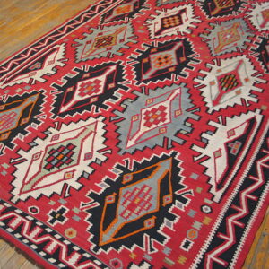 Flatweave runner in red, black, gray, and white with large serrated geometric medallions on worn wood flooring.