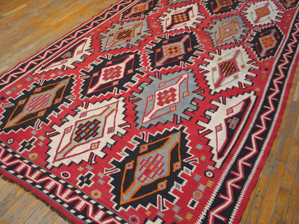 Flatweave runner in red, black, gray, and white with large serrated geometric medallions on worn wood flooring.