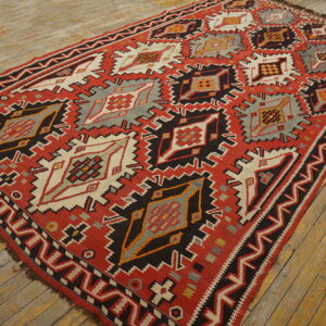 Red, black, gray, and cream flatwoven rug with large serrated geometric patterns on distressed wood planks.