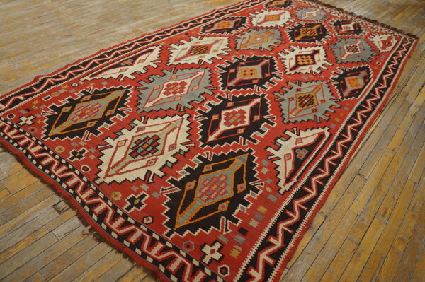 Red, black, gray, and cream flatwoven rug with large serrated geometric patterns on distressed wood planks.