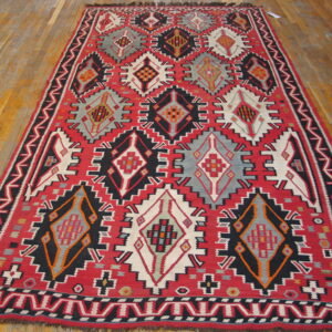 Geometric red, black, grey, and white flatweave rug with diamond patterns on a plank wood floor.