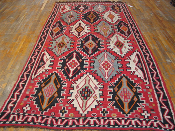 Geometric red, black, grey, and white flatweave rug with diamond patterns on a plank wood floor.