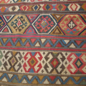 Flatweave rug with colorful geometric bands and stepped diamonds rests on honey-toned wood floor.