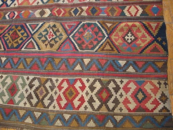 Flatweave rug with colorful geometric bands and stepped diamonds rests on honey-toned wood floor.